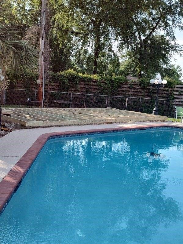 A large swimming pool is surrounded by trees and a fence.