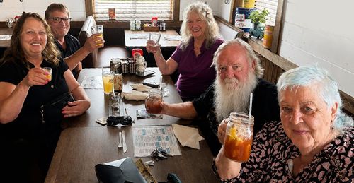 Group of people at a table in a café, smiling and raising drinks in a friendly toast.