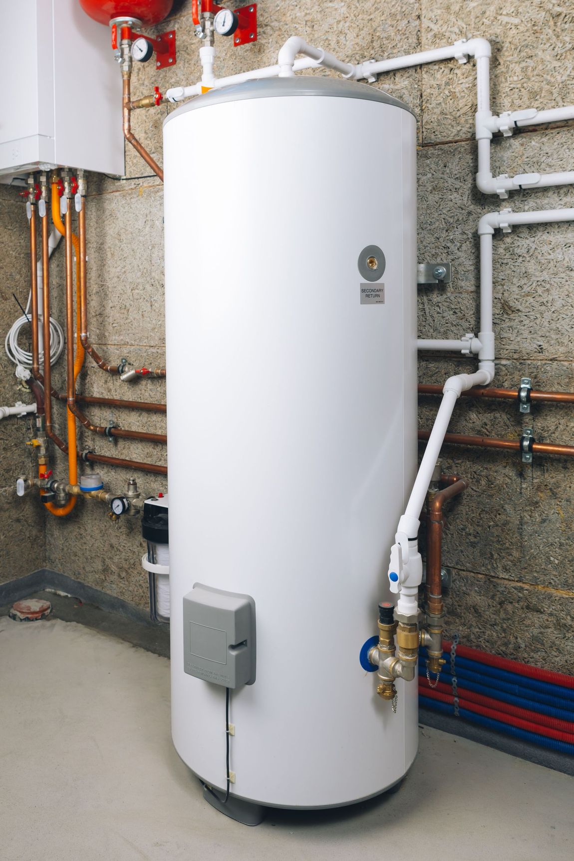 White water heater in a basement with connected pipes and other plumbing fixtures.