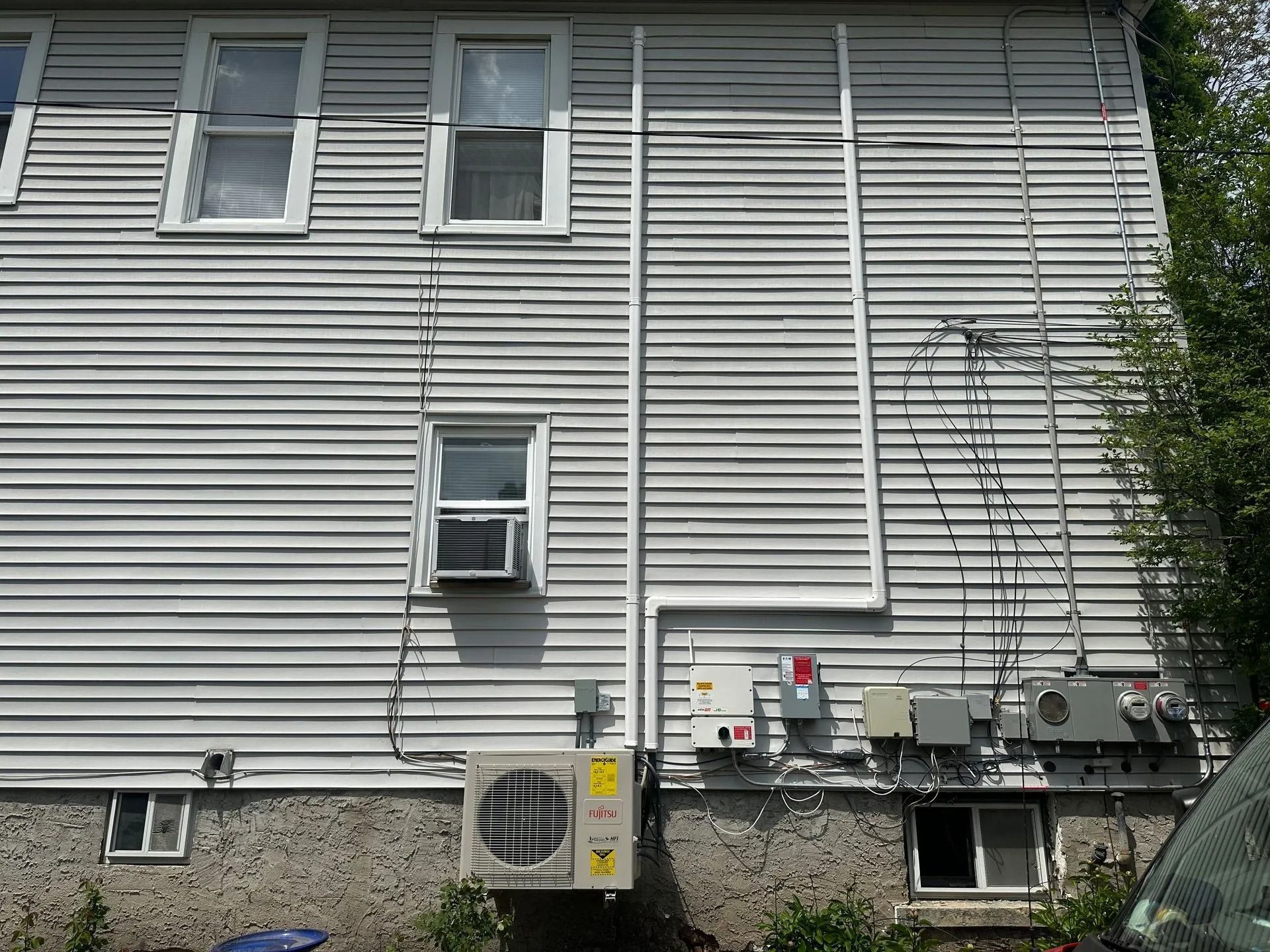 Exterior of a gray building with air conditioning units, electrical boxes, and windows.