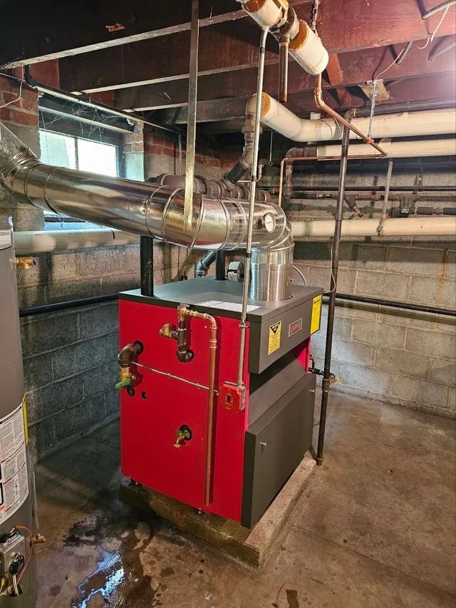 Red and gray furnace with pipes in a basement.