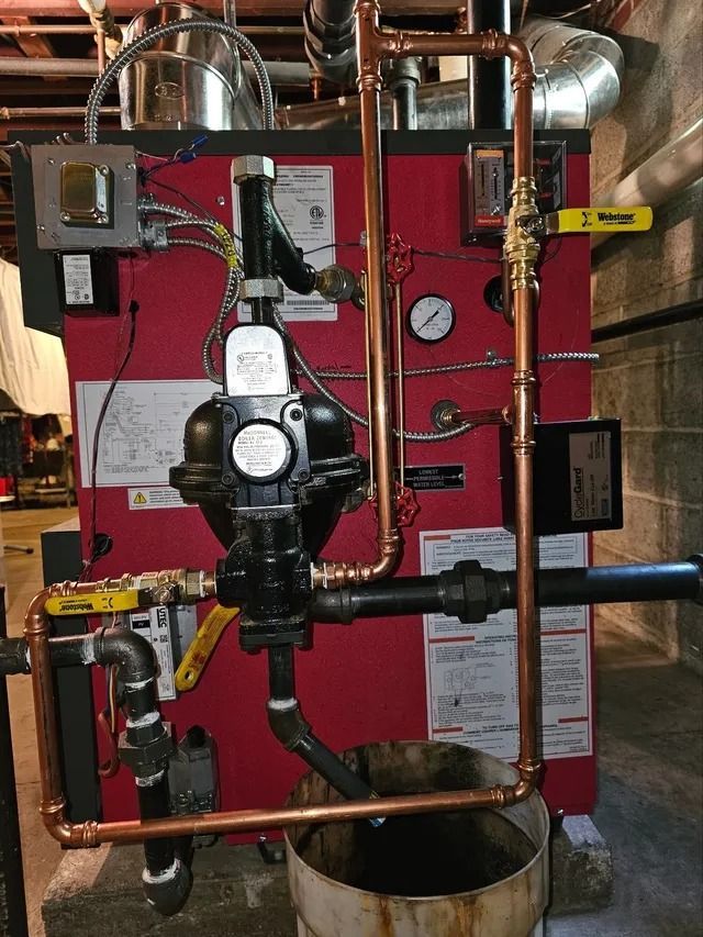 Red boiler with copper pipes, valves, gauges, and a bucket.