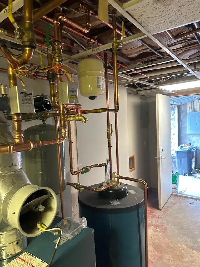 Copper pipes and expansion tank connected to a blue water heater in a basement.