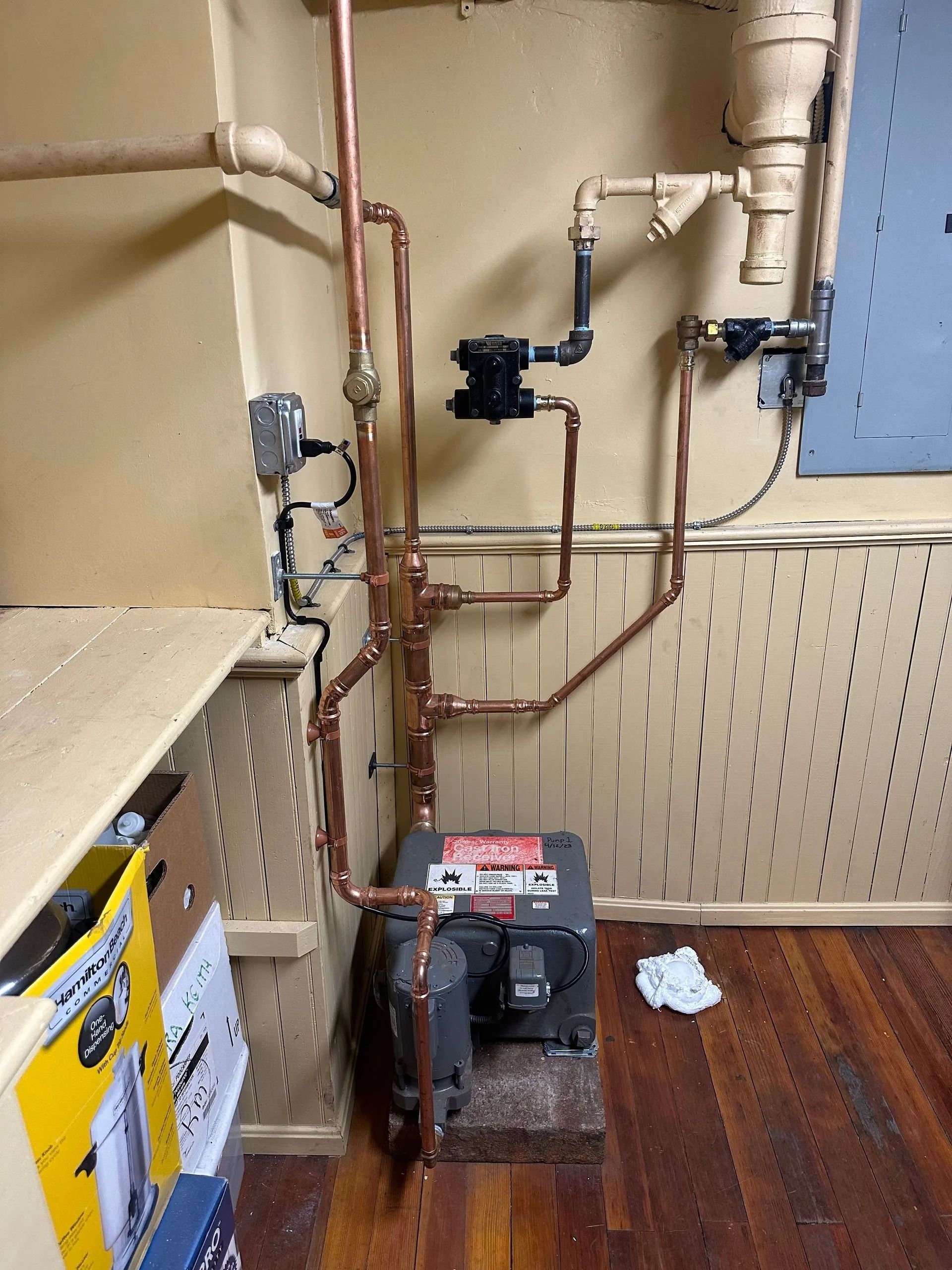 Copper pipes and plumbing, likely for heating, against a wall. A machine sits on the floor.