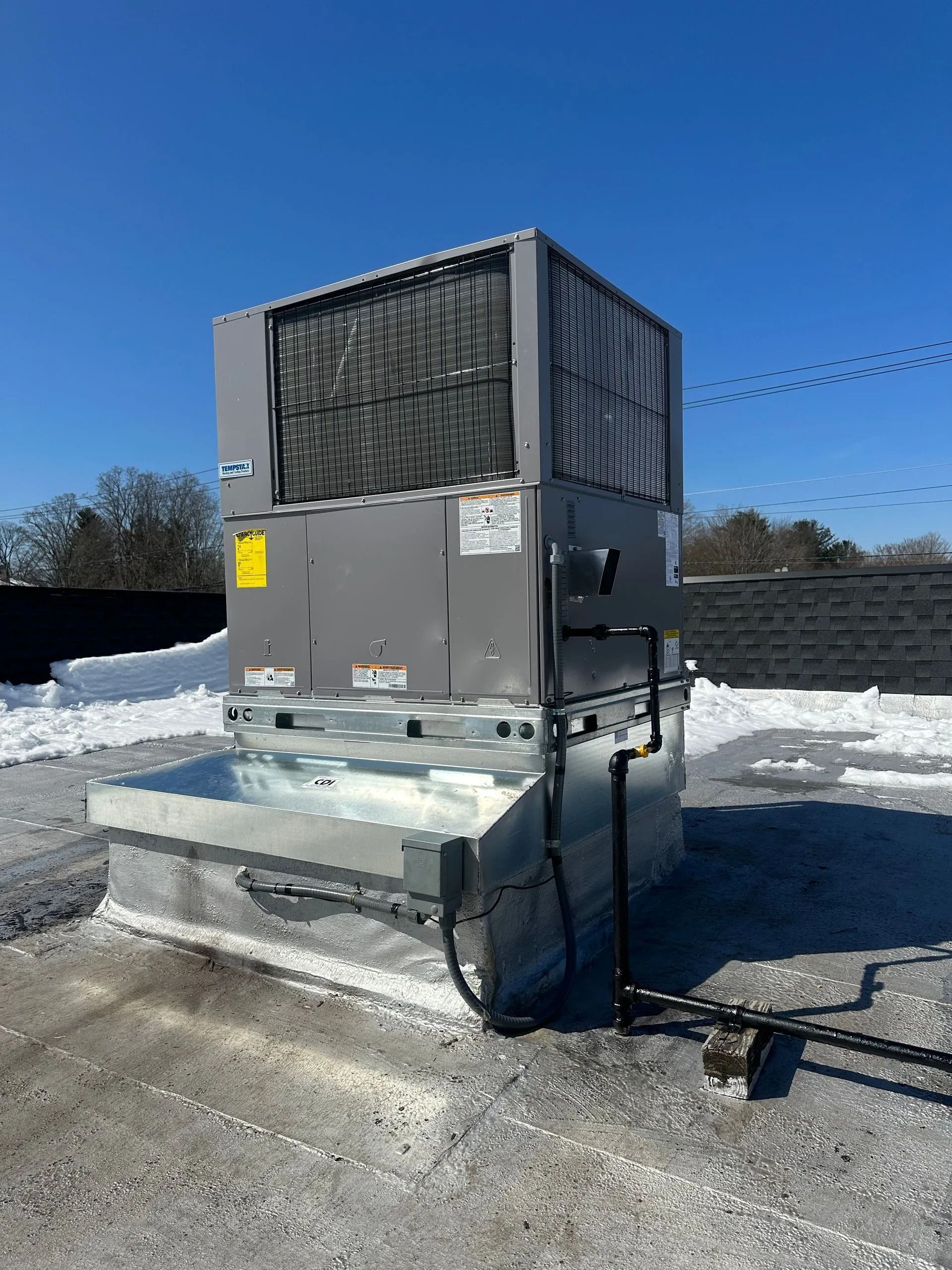 Rooftop HVAC unit on a building with snow. Gray metal with dark vents. Clear blue sky.