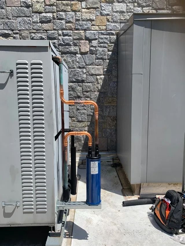 HVAC unit with copper pipes and a blue filter attached to an exterior wall.
