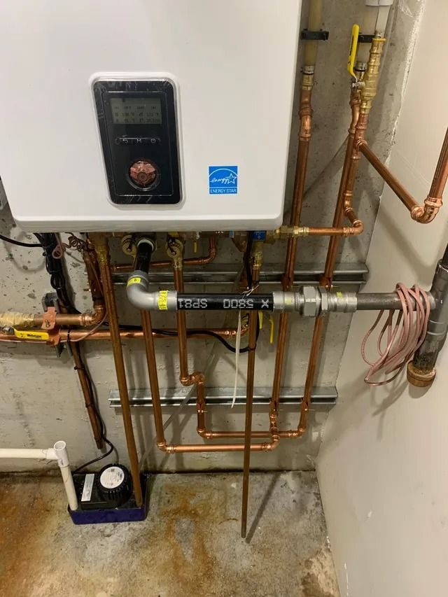 Wall-mounted water heater with copper pipes in a basement setting.