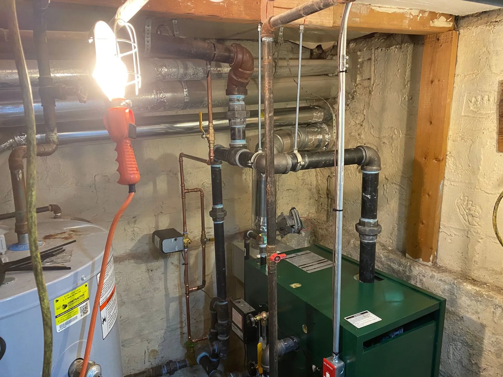 Green boiler with copper pipes, wiring, and a work light in a basement setting.