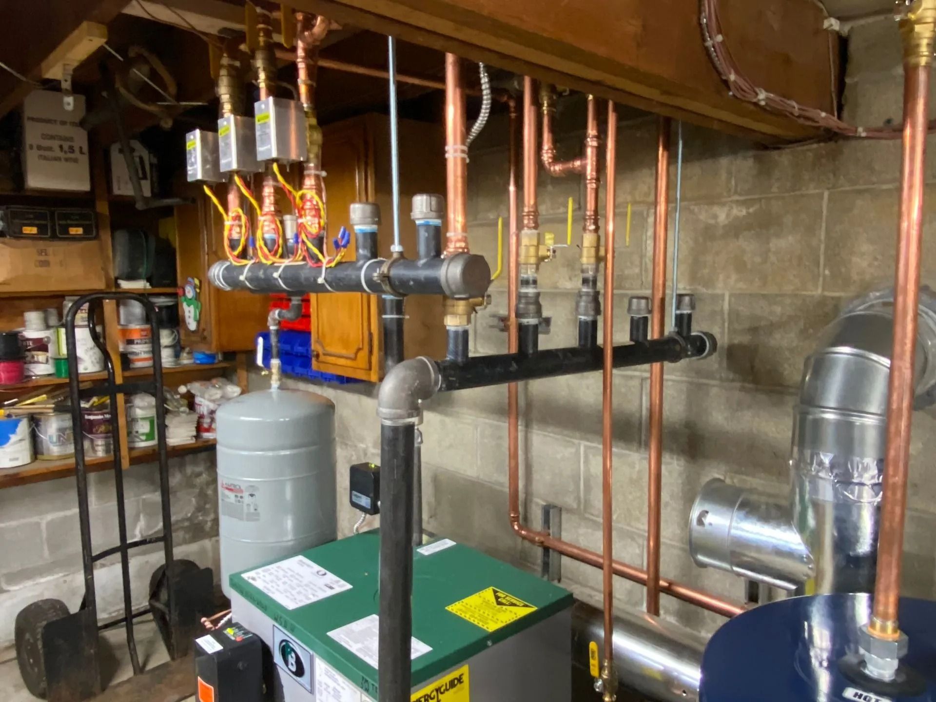A basement with a boiler system and copper pipes attached to a water heater and various electrical components.