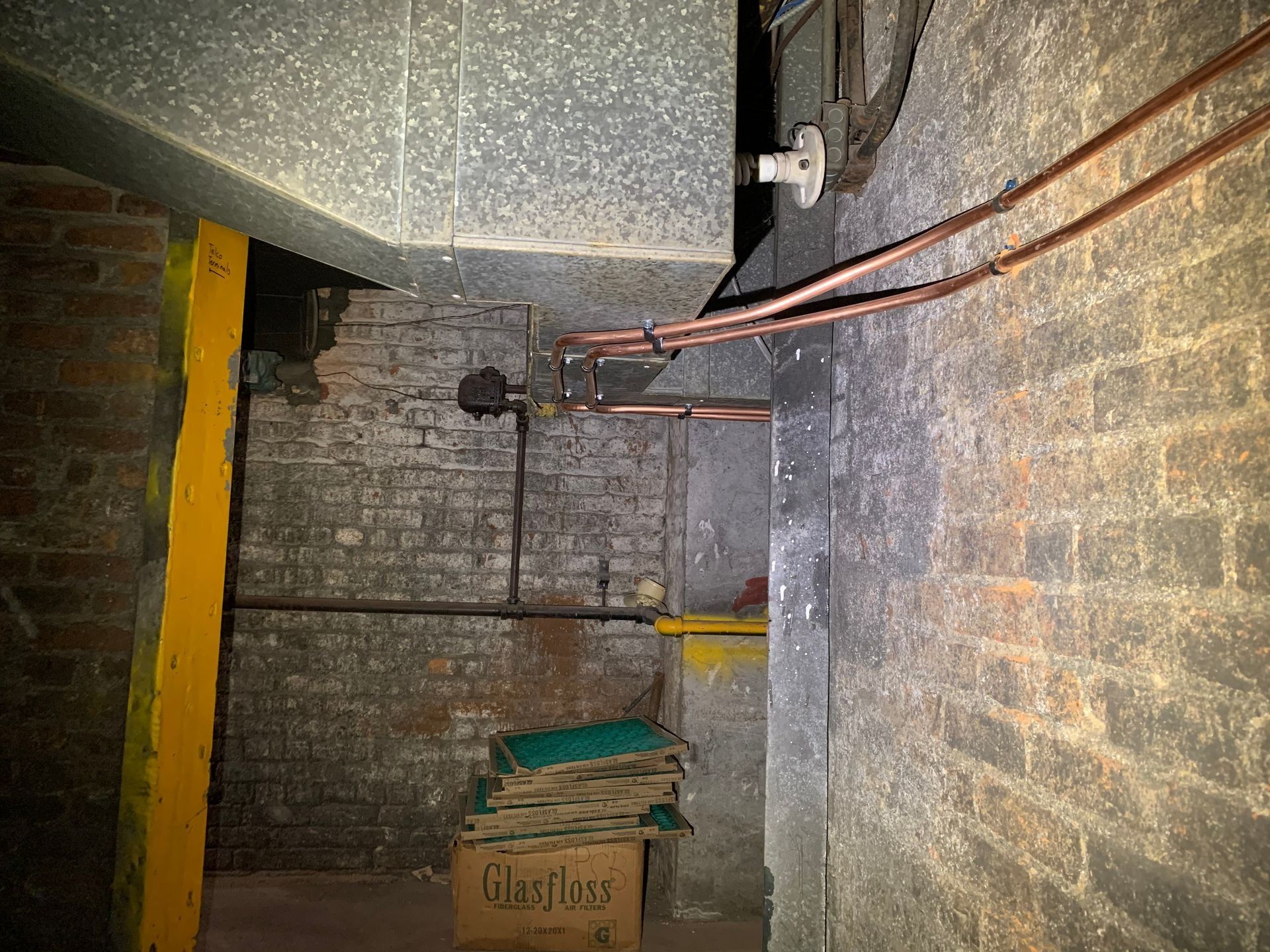 Basement with exposed brick walls, copper pipes, ductwork, and support beam.