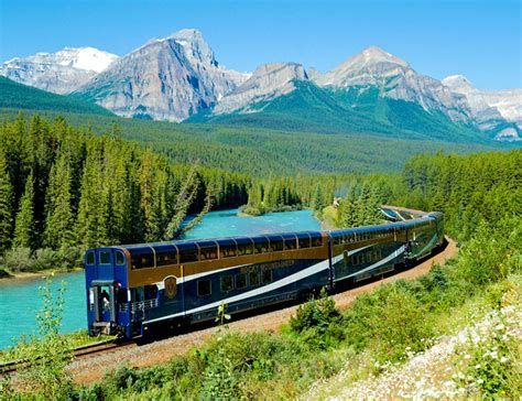 Canadian Rockies Rocky Mountaineer train is going through a forest with mountains in the background.