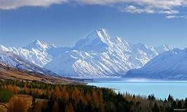 A mountain covered in snow is surrounded by a lake and trees