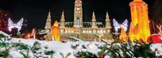 A castle is lit up at night with christmas decorations in front of it.