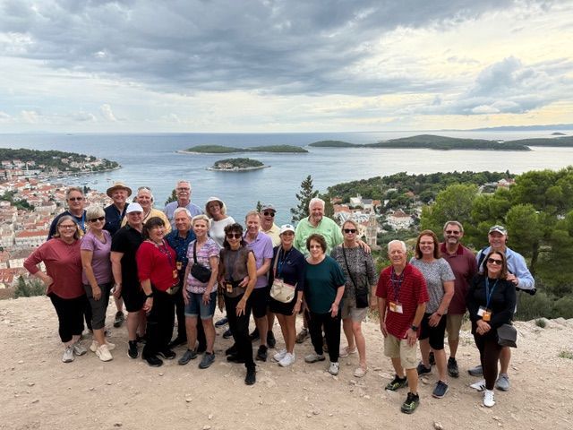 Group of tourists overlooking coastal town with islands in the distance under a cloudy sky.