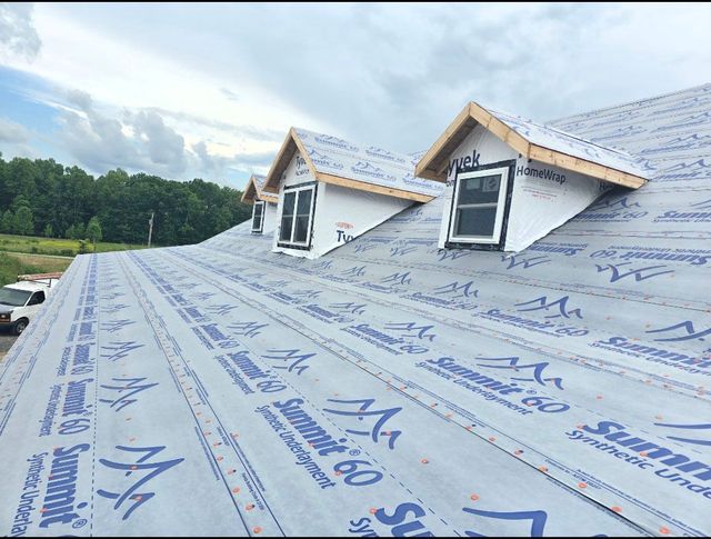 Roof under construction with blue protective underlayment and two dormer windows on a cloudy day