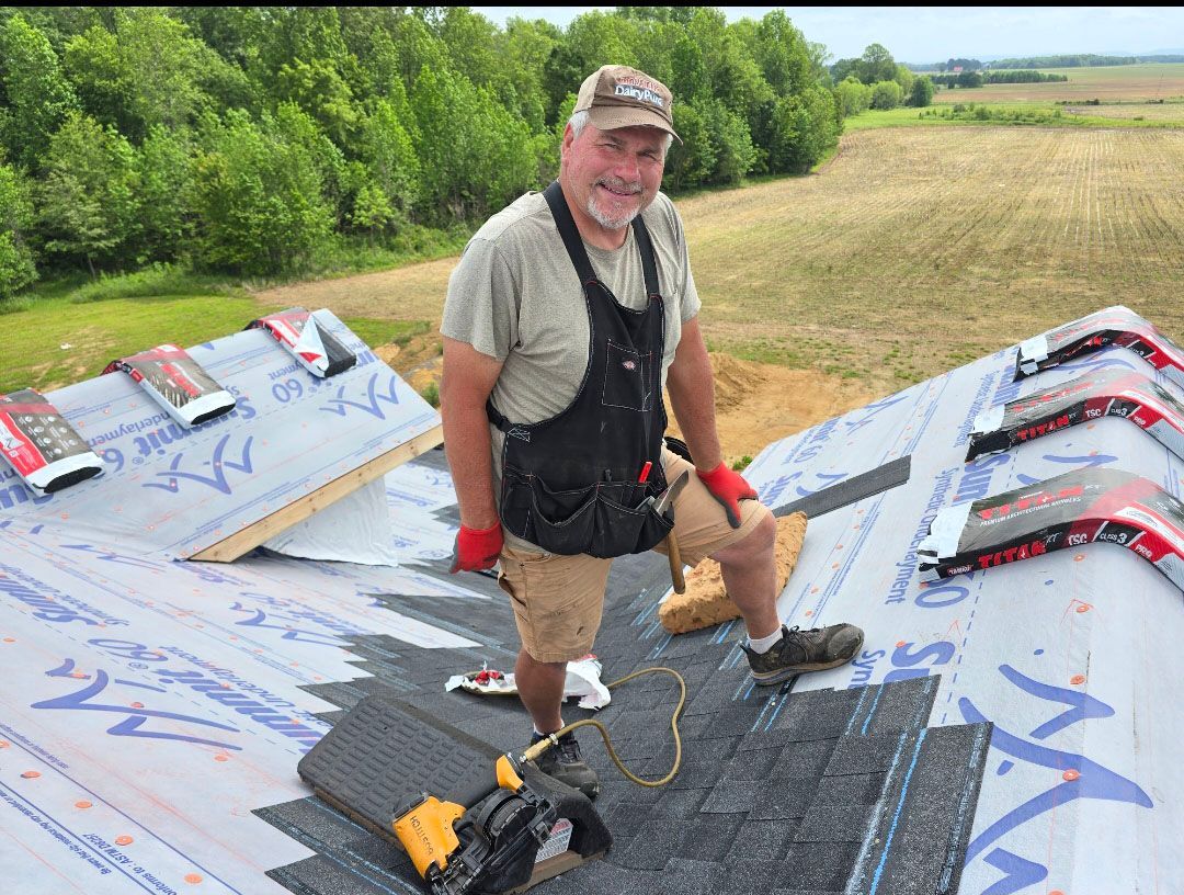 Man standing on a wing-like roof, holding tools, with a grassy field and trees behind him.