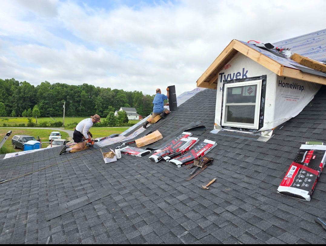 Workers installing shingles on a steep roof during home construction, with materials scattered on the roof.