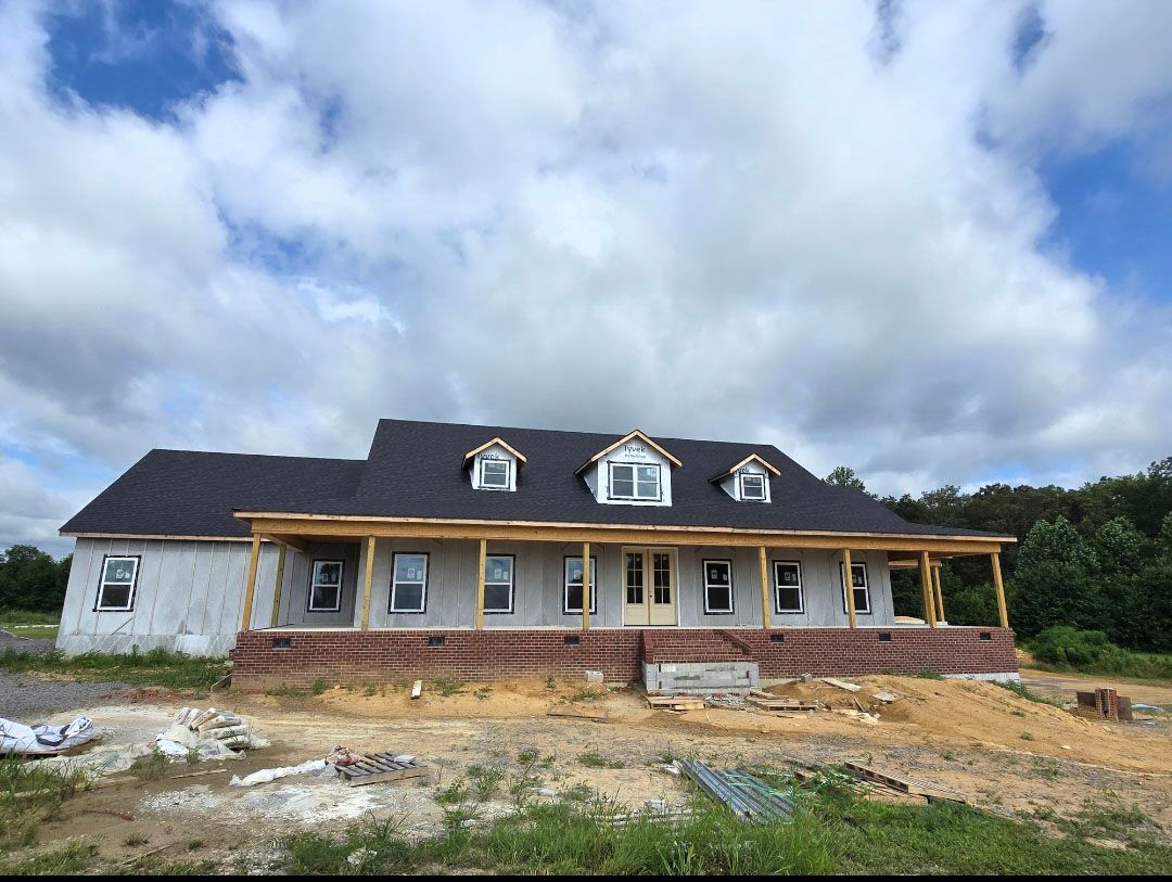 Partially built white house with dark roof, front porch, and brick steps under a cloudy sky.