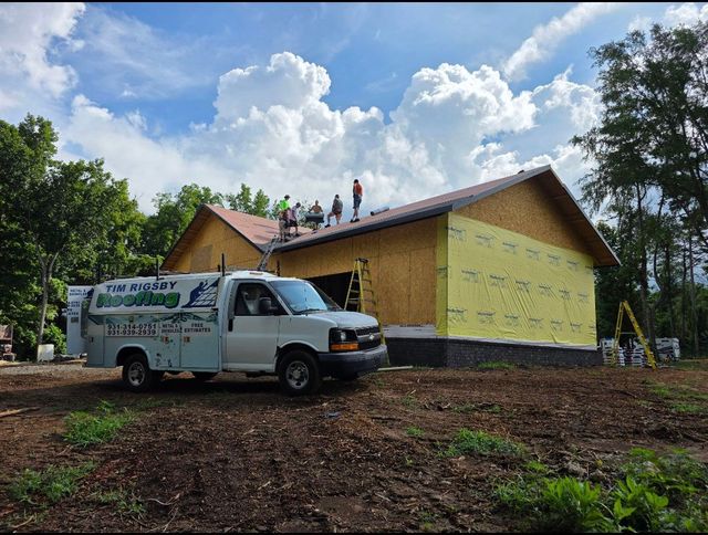 White work truck parked beside a yellow house under construction on a dirt lot, with workers on the roof.