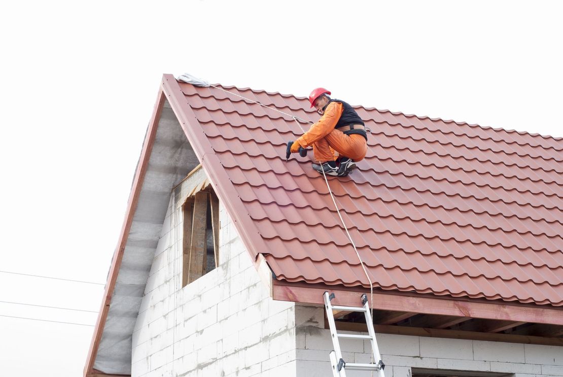 Worker in orange safety gear repairing a red-tiled roof beside a ladder