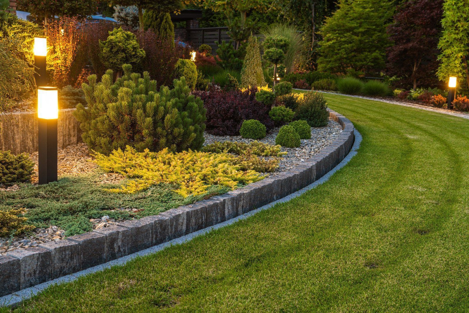 Lit garden path curving past landscaped shrubs and flowers at dusk