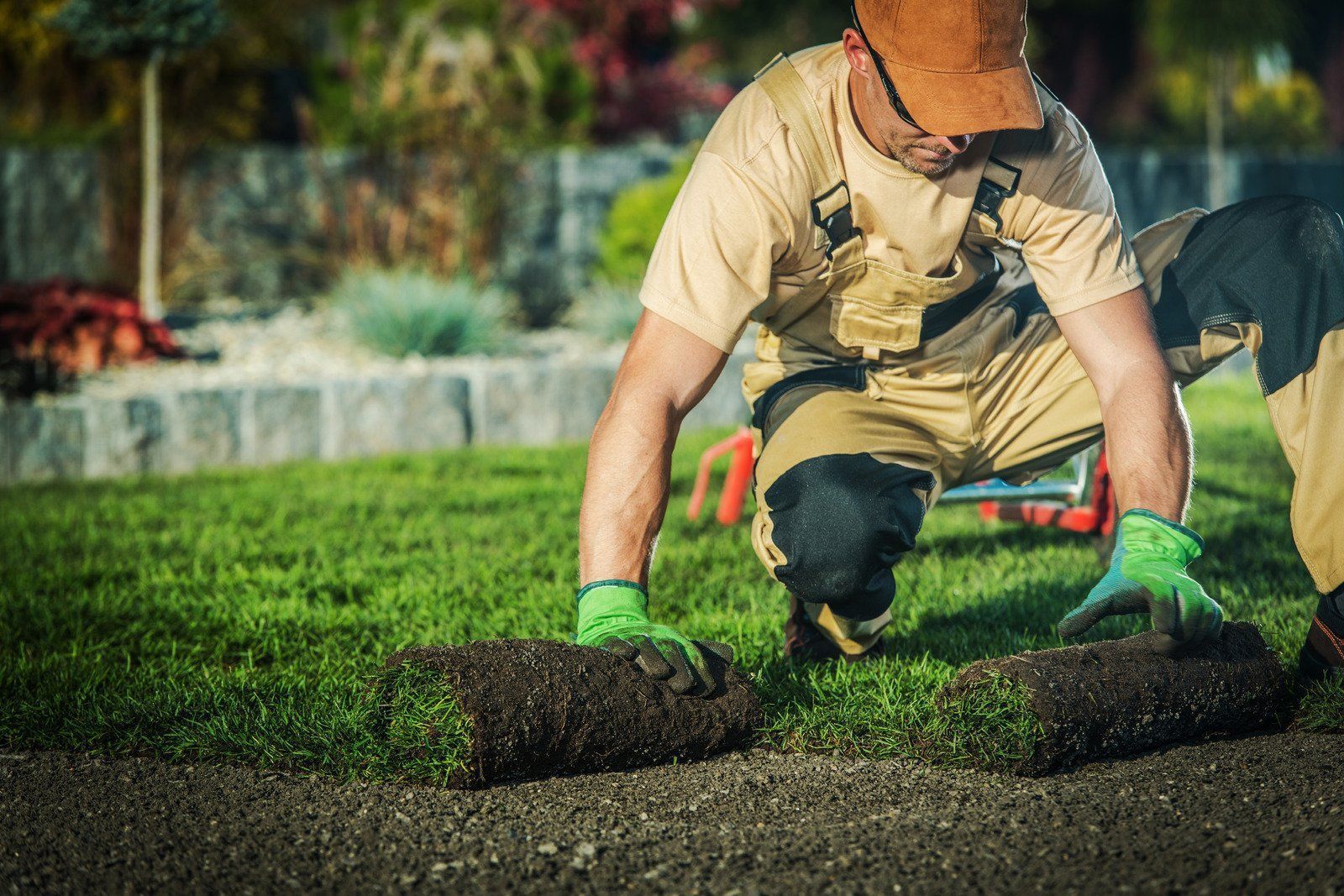 Worker laying fresh sod on a lawn with a trowel, wearing green gloves and overalls