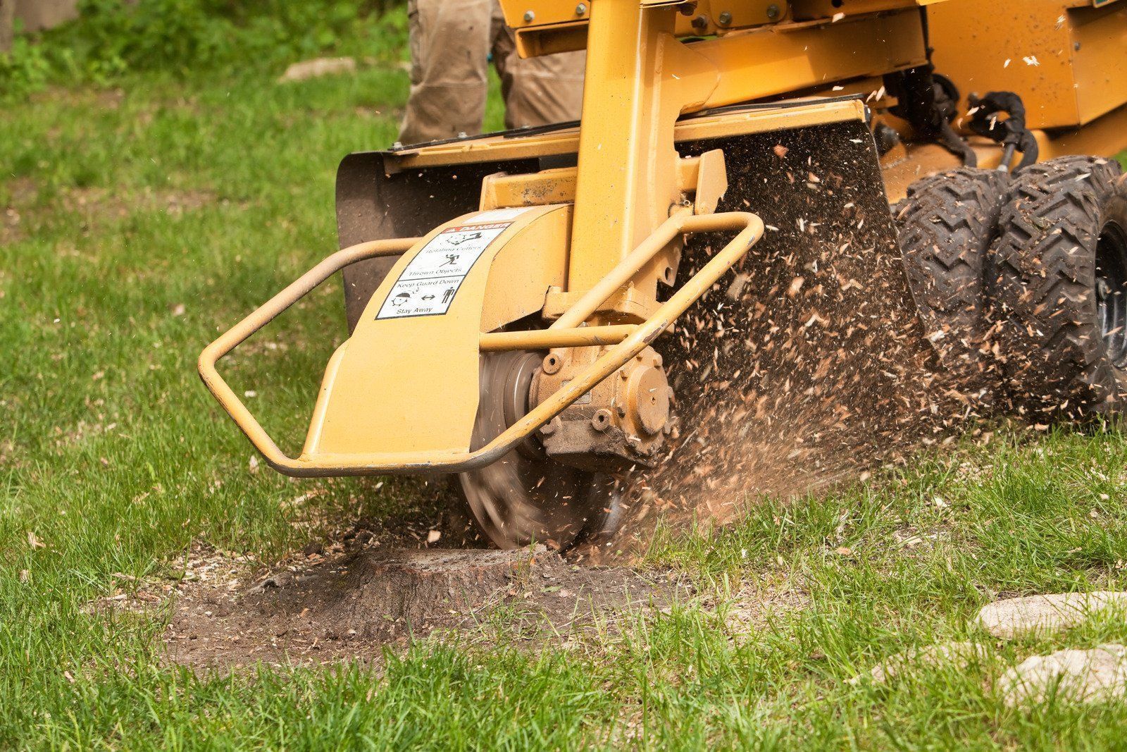 Yellow wood chipper ejecting debris on grass near a tractor wheel