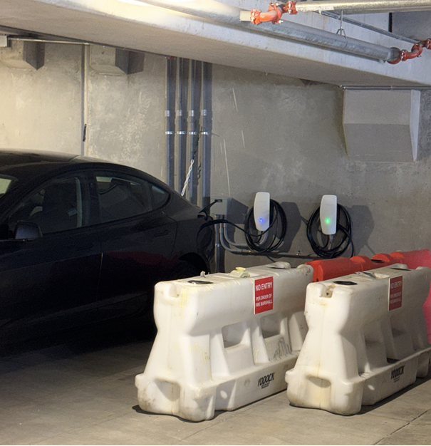 Parking garage with a black car, two EV chargers, and white barriers in front of concrete walls.
