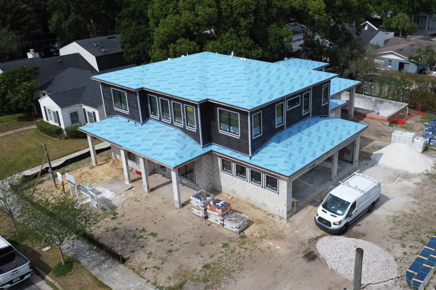 Aerial view of a two-story house under construction with a blue roof and a white van parked beside it.