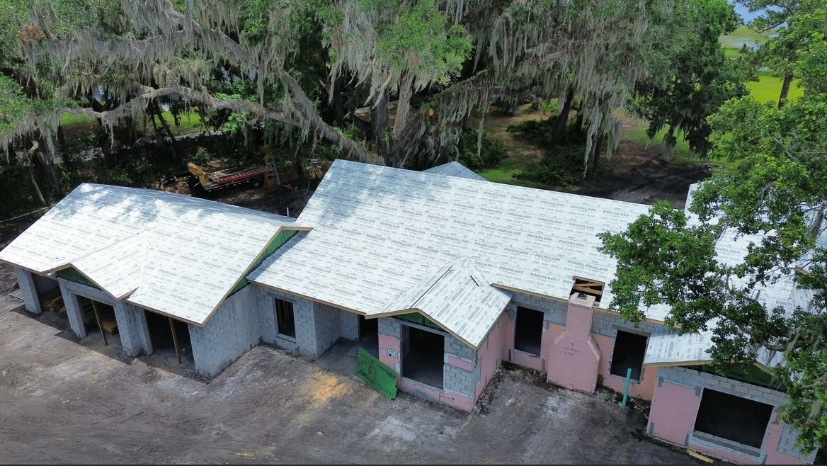 Aerial view of three small white-roofed buildings beside trees and dirt ground.