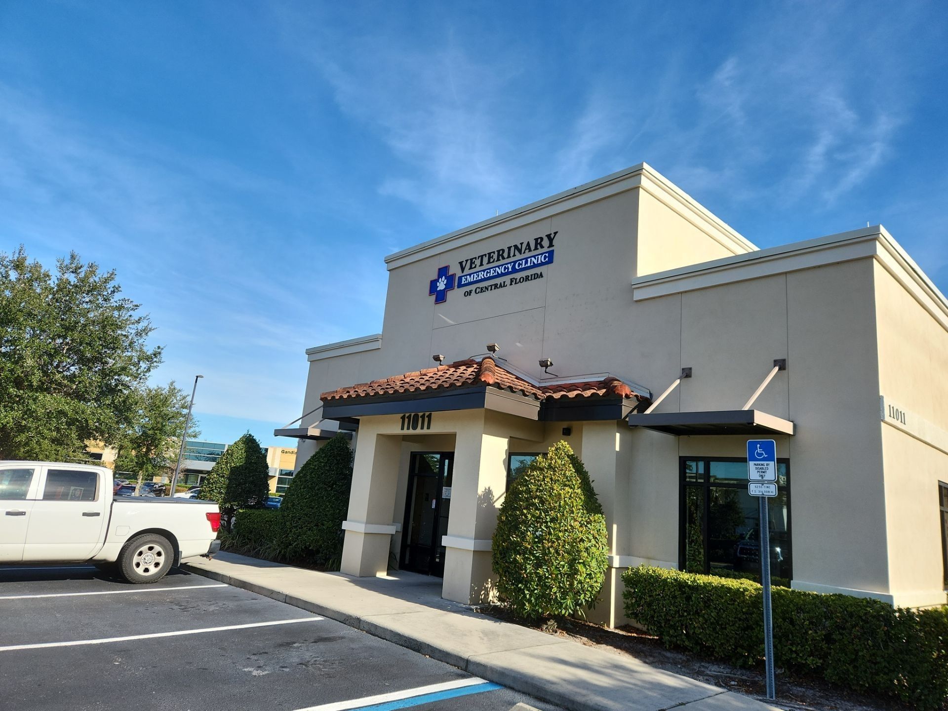 Exterior of a beige commercial building with a blue sign, parking lot, and a white truck under a clear sky