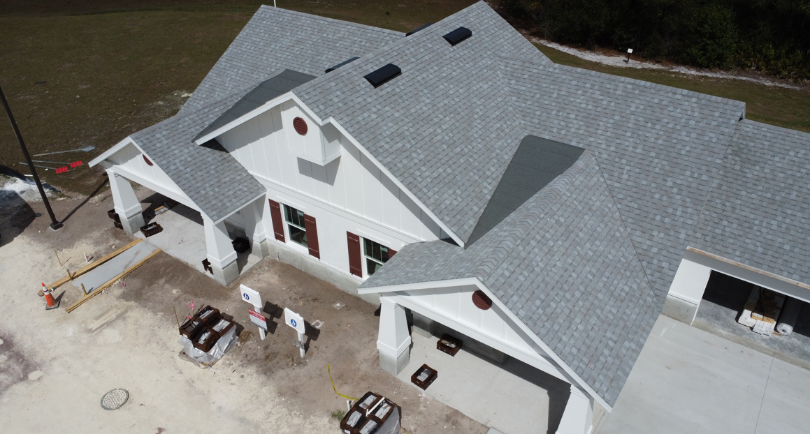 Aerial view of a white house with gray shingle roof and front porch under construction