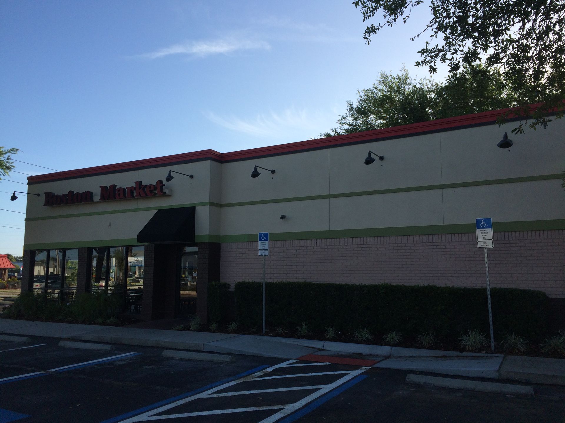 Storefront of a strip mall with red trim, green awning, and parking spaces in front