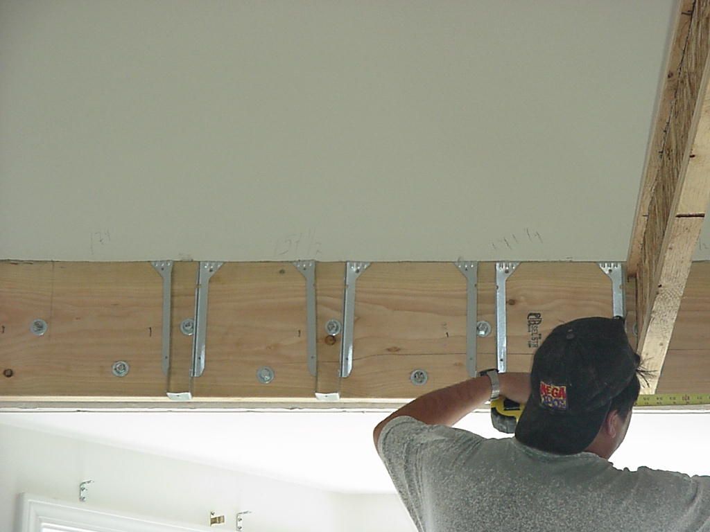 A man is measuring a ceiling with a tape measure.