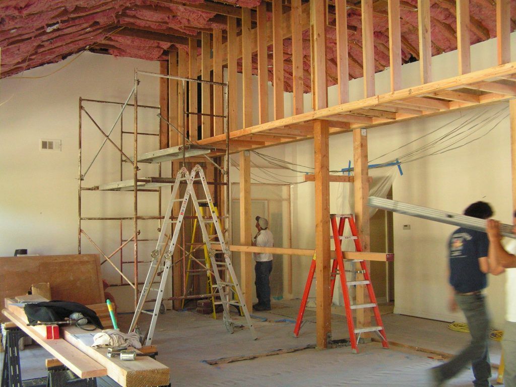 A man is carrying a ladder in a room under construction