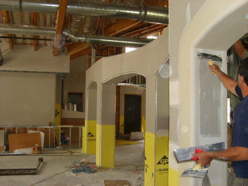 Two men are plastering a wall in a building