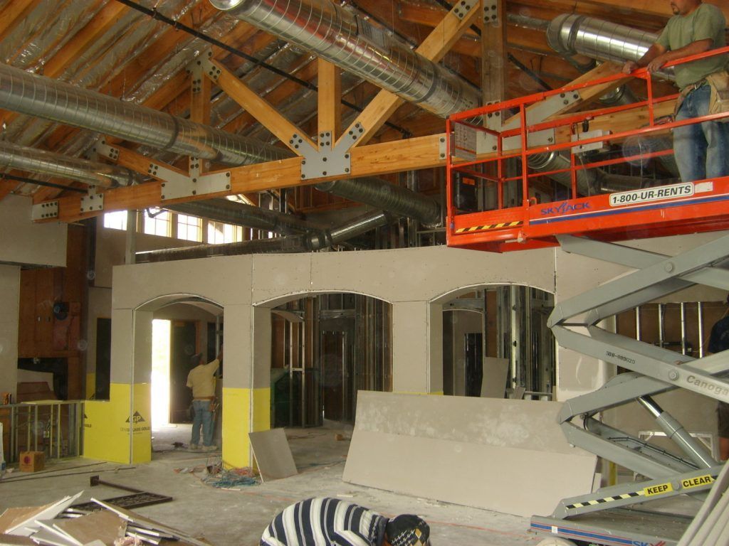 A man in a striped shirt is kneeling in front of a scissor lift