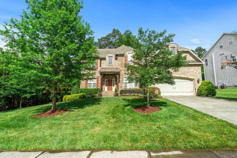 A large house with a lush green lawn and trees in front of it.