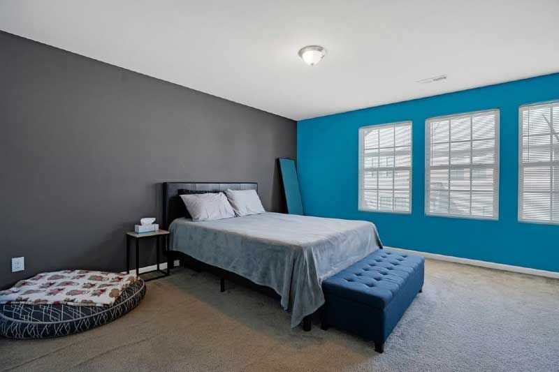 A bedroom with a bed , ottoman , and blue walls.