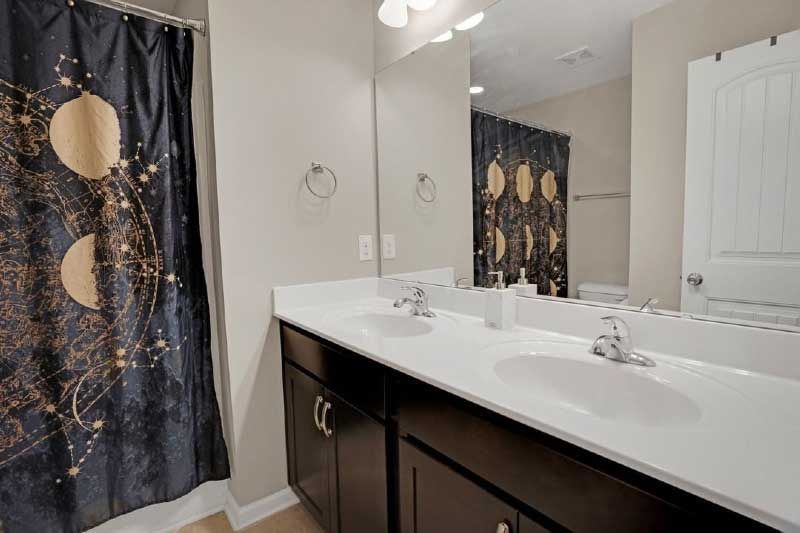 A bathroom with two sinks , a shower curtain and a mirror.
