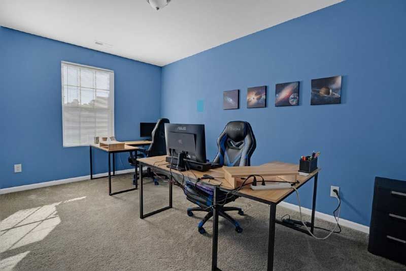 A room with blue walls and two desks with computers on them.