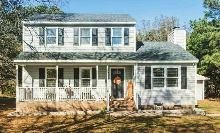 A white house with a large porch and a man standing in front of it.