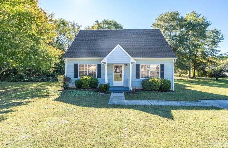 A small white house with a black roof is sitting on top of a lush green field.