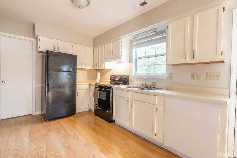 A kitchen with white cabinets , a black refrigerator , a stove , and a sink.