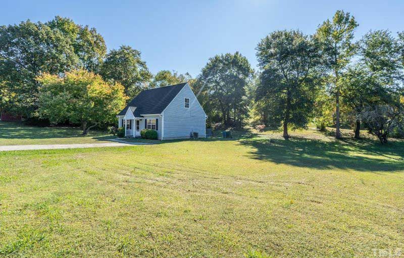 A small white house is sitting in the middle of a lush green field surrounded by trees.