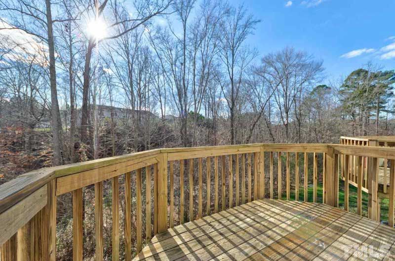 A wooden deck with trees in the background and the sun shining through the trees.