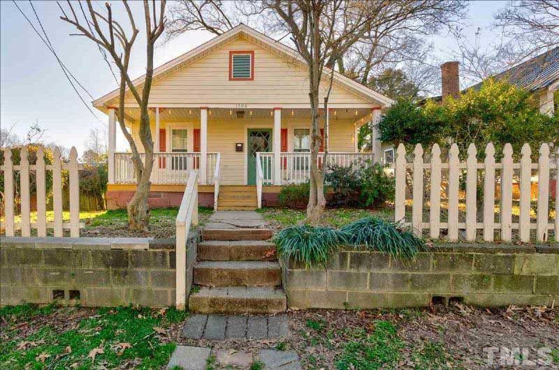 The front of a house with a white picket fence and stairs leading to it.