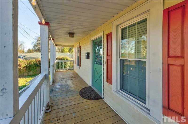 The front porch of a house with a green door and red shutters.