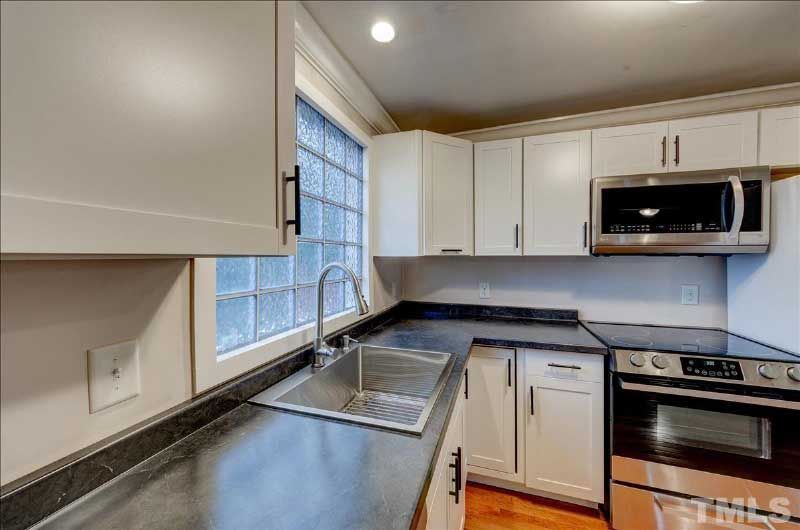A kitchen with white cabinets , stainless steel appliances , a sink and a microwave.