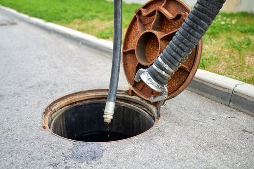 Open manhole with hose and lid on asphalt pavement.